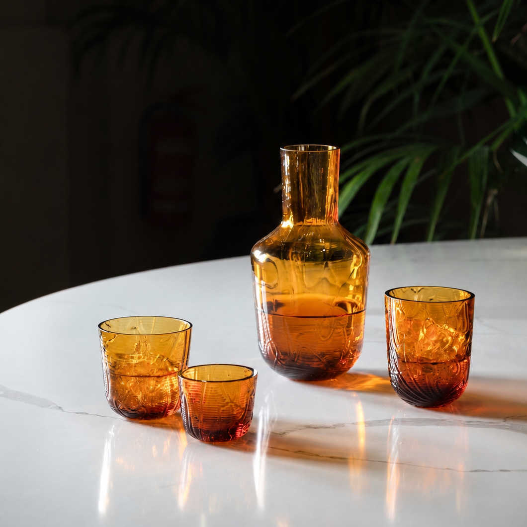 Set of amber glassware including a carafe and three glasses on a reflective surface with a dark background.
