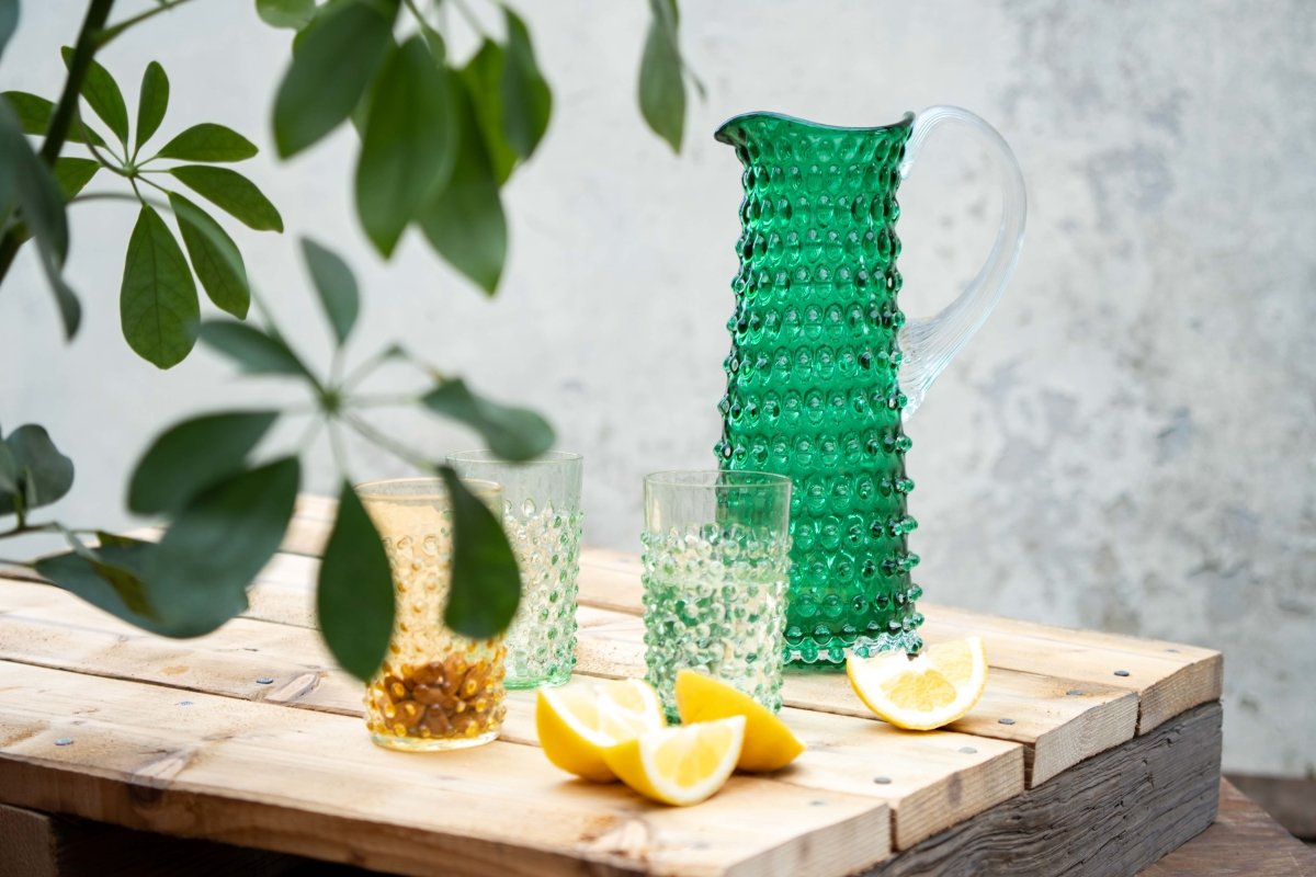 Underlay Dark Green Hobnail Jug Tall on a wooden pallet, surrounded by products from the Hobnail and lemon collections, with a concrete wall in the background