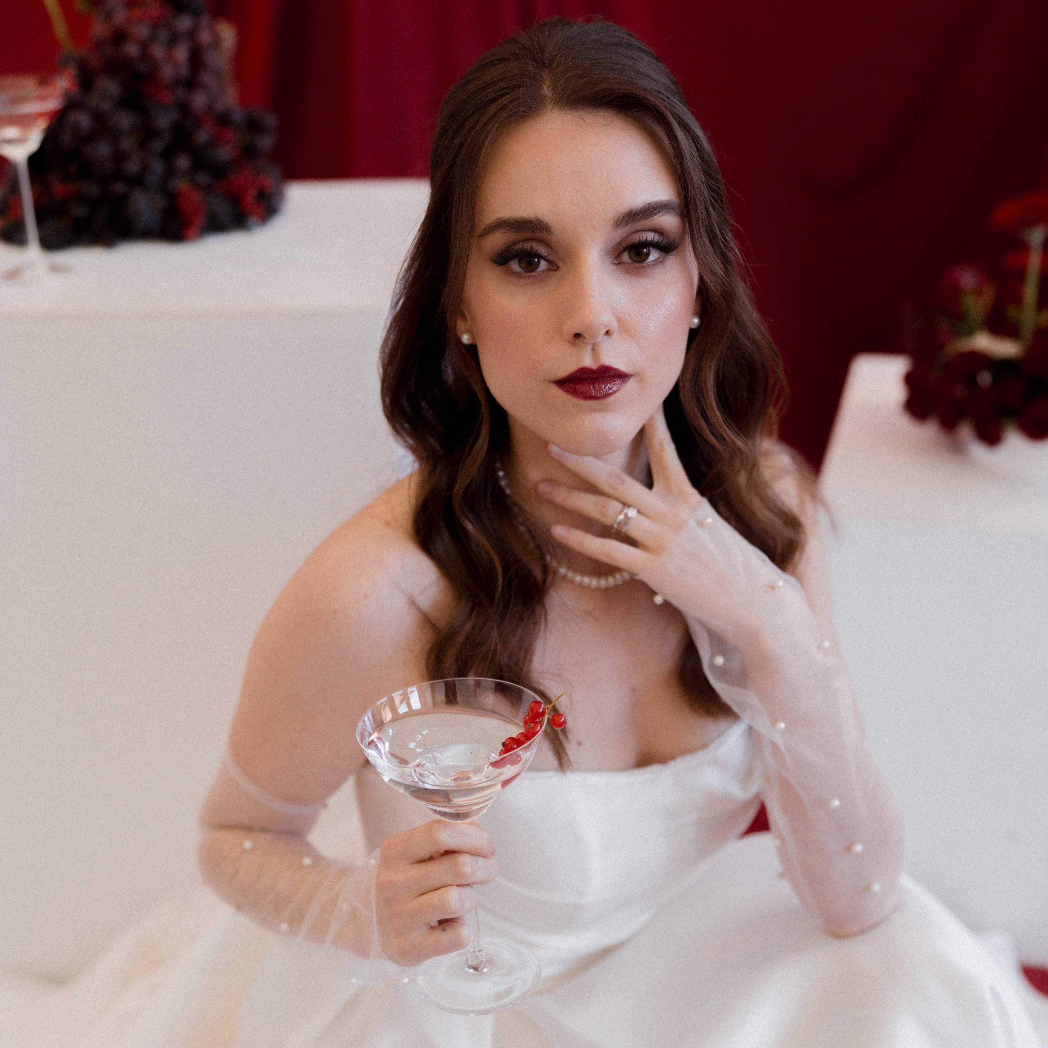 Woman in a white dress holding a cocktail glass with a red background